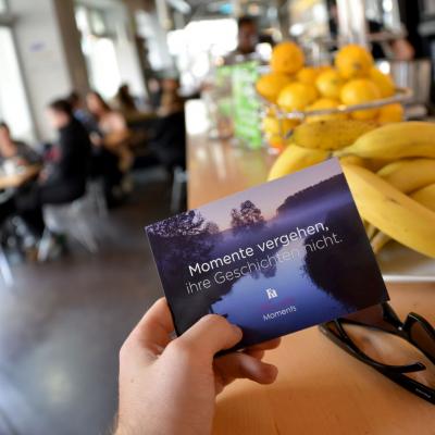 Hand hält in schickem Bar Restarant blau Werbe Postkarte für Fa vor braunem Holz Tresen