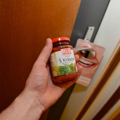 Hand mit Glas Felix Tomaten Sugo vor Tür mit Werbeanhänger an der Klinke