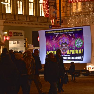 beleuchtetes 16 Bogen Plakat auf weissem Auto mit Werbung für Afrika! Afrika! nachts im Großstadtverkehr