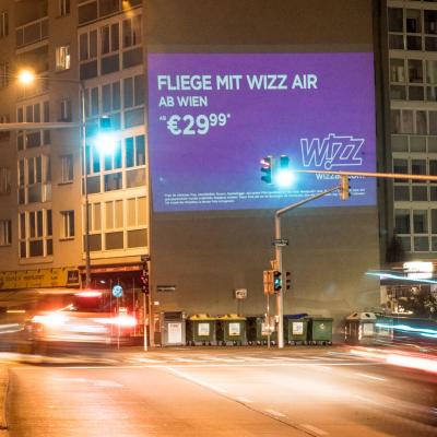 Projektion mit Werbung für Wizz Air auf Fassade in Großstadt in der Nacht