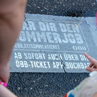 Passanten sehen auf dem Boden Werbung für ÖBB Sommer Tickets